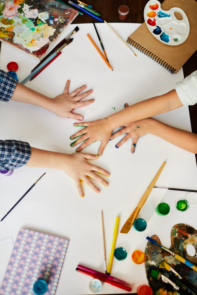 Above view of children's hands with paint and school supplies showing educational services and special education services