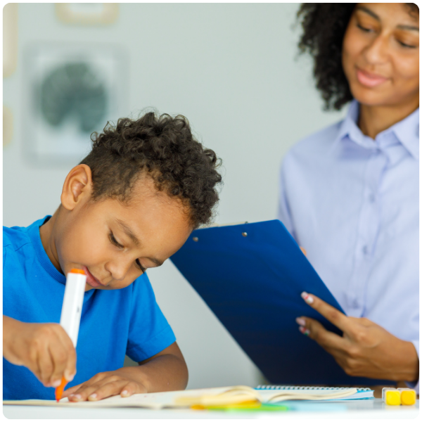 Little boy drawing with therapist watching over him demonstrating the ABA therapy services integrated into the educational services